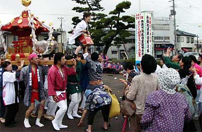 JR燕駅前で行われた燕1000人みこしのPRみこしで、みこしの上からモチをまく、よさこいソーランのグループのメンバー