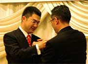 渡辺新理事長(左)と韮沢前理事長のバッジ交換