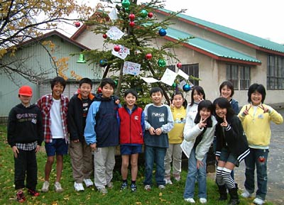 条南小学校中庭に仮設住宅から移植されたモミの木の飾り付けを終わった児童ら