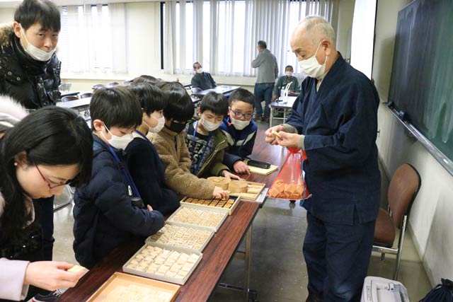 2月26日の「わくわく文化未来塾」のジュニア将棋教室で子どもたちに竹風駒を見せる大竹日出夫さん