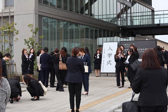 入学式の看板と並んで写真を撮る新入生の行列ができる