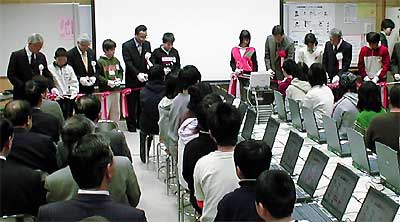 ノートパソコンの並ぶコンピューター教室でテープカット