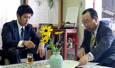 ジンバブエの資料を前に話す高橋燕市長（右）と歓談する小沢直義さん（左）