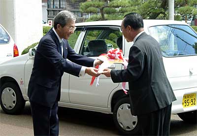 高橋甚一燕市長（右）に車のキーを手渡す高橋作衛理協栄信用組合理事長（左）