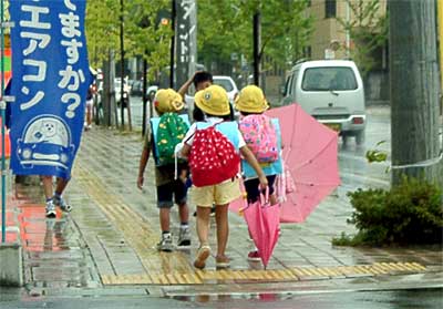三条市旭町2地内の歩道で傘を差したり閉じたりして学校から帰る小学生