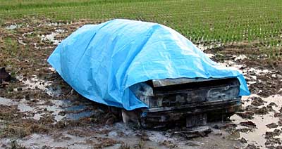 青いビニールシートがかけられ、黒こげになった車