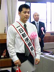 たすきをかけて一日郵便局長を務めるミヤザワタケシさん