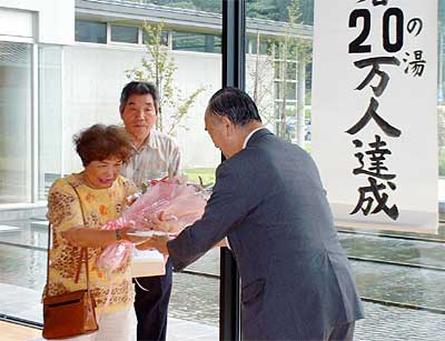 キャプション加茂市市民福祉交流センター「加茂美人の湯」の入館20万人目となり、小池市長から花束を受け取る川崎陽子さん