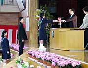 鉢植えの花で飾ったステージに上がって今井校長から卒業証書を受け取る卒業生