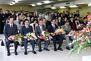 花束を手に退職者市長のあいさつを聞く退職者