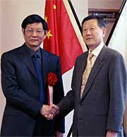 両国国旗を背に握手する謝鄂州市長と高橋三条市長