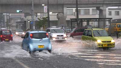 東北電力三条営業所前で冠水した市道旭町通り線を水しぶきを上げて走る車