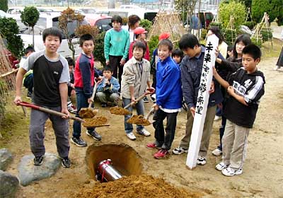 燕西小学校の児童玄関前の前庭にタイムカプセルを埋める児童