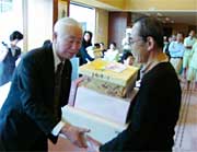 両手に持ちきれないほどのプレゼントを受け取る100万人目の植村さん