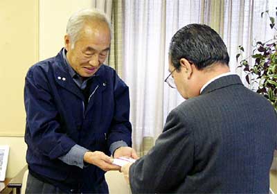 高橋燕市長(右)に30万円の小切手3枚を包んだのし袋を手渡す平田平田商事(株)社長(左)