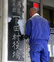 「新潟県南蒲原郡　下田村」の銘板のまわりのセメントを削り…