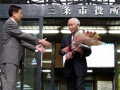 退庁する市長職務執行者だった佐藤氏（右）に握手を求める高橋市長（左）