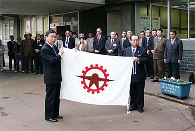 燕市役所玄関前の市旗を降ろして広げて見せる中野助役(左)と高橋市長(右)