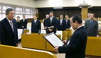 起立した市議の前で代表の川上議長に感謝状を贈る高橋市長