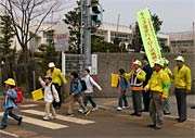 貸与された防犯活動用グッズを装着して大崎小前の横断歩道に立つ三条市大崎地区自治会長協議会