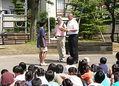 19日、条南小学校で行われたモミの木のメモリアルプレート贈呈式で、児童にプレートを手渡す丸山燕三条青年会議所理事長(左)