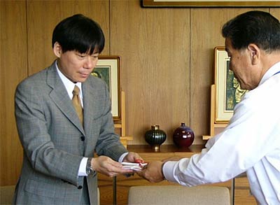 小林燕市長(右)に500万円を手渡す故吉川嘉之さんの長男、力さん(左)