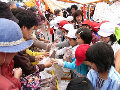 27日、二七の定期市でにぎわう中央市場で懸命にサツマイモを売りさばく飯田小3年生