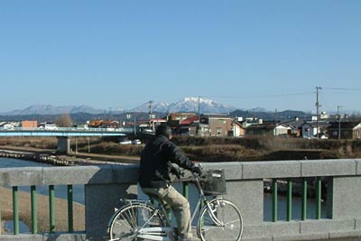 自転車を止めて常盤橋から粟ヶ岳を眺める市民