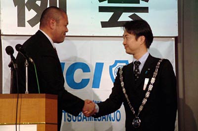 バッジを交換して握手する丸山直前理事長(左)と小林理事長(右)