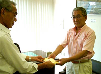 三条市社会福祉協議会の岩本事務局長(左)に11,520円を手渡す県央食品衛生協会三条支部の佐野支部長(右)