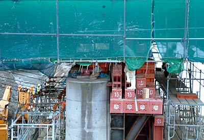 旧橋のジャッキアップが行われている御蔵橋、コンクリートの橋脚の内側(右)に鉄骨の足場を組んだ上に載せた油圧式ジャッキで上の橋脚を持ち上げる