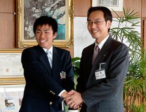 青年海外協力隊員としてアフリカのザンビア共和国に派遣される渡辺さん(左)と握手する国定市長(右)