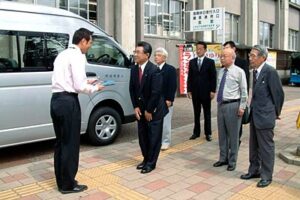 寄付したワンボックスカーの前で国定三条市長(いちばん左)にキーや車検証を渡す三条南ロータリークラブの坂本会長(左から2番目)