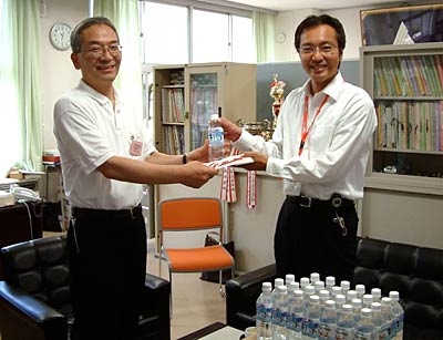 国定三条市長(右)から市が新潟県央工高野球部を甲子園に送る会にプレゼントする三条市のミネラルウオーター「千年悠水」500mlボトル4,000本の目録を同会事務局の梨本正實事務局長(左)に手渡す