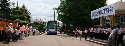 10日ぶりに学校に戻るナインを乗せたバスを小旗を振り、拍手で迎える