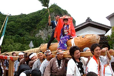 23日開かれた「しただふるさと祭り」、八木ヶ鼻を背に進む雨生の大蛇の行列行進