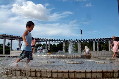真夏同然の猛暑に三條機械スタジアム前の噴水で水遊びする子どもたち