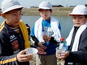 自分たちで育て稚魚のコップを持つ児童