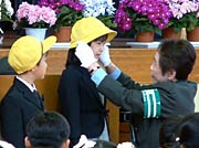 交通指導隊員から黄色い帽子をかぶせてもらう1年生