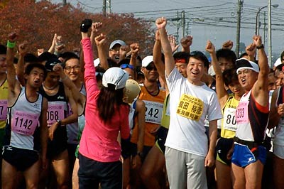 拡声器を手にスタート前のランナーを激励する千葉さん、一緒に右手を上げてこたえる泉田知事