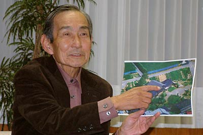 加茂市役所で寄付する土地の航空写真を手に小池市長に話す関川さん