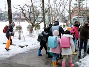 雪にすっぽりと覆われたグラウンド横目に下校する児童