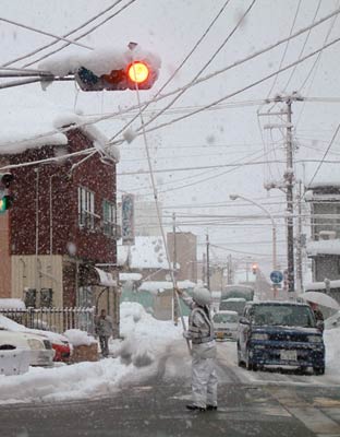 雪落とし棒で信号機の雪を落とす警察官