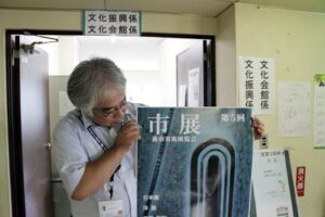 燕市展事務局の燕市教育委員会生涯学習課文化振興係で市展ポスターを手に出品を呼びかける担当職員