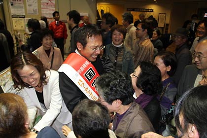 会場を出る来場者にもみくちゃにされながら握手をして送る国定夫妻