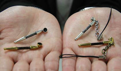 燕市産業史料館のミュージアムショップで販売しているミニチュアの煙管のアクセサリー、向かって左がピンバッジ、右がチャーム、上がシルバー、下が真ちゅう