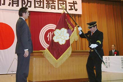 国定市長から消防団旗を受ける長谷川団長