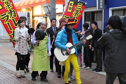 ギターを弾いて歌いながら昭栄通りを進む撮影のようす