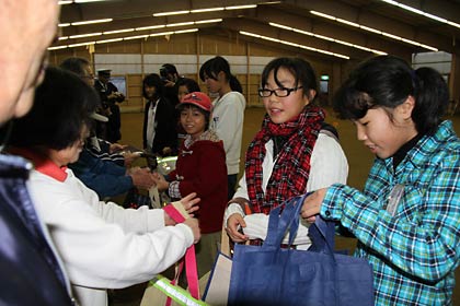 ゲートボール場でお年寄りにエコバッグを手渡す子どもたち