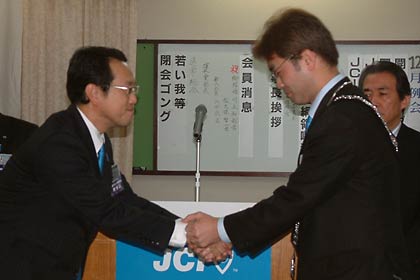 加茂青年会議所の牛腸理事長(左)からプレジデンシャルリーフと理事長バッジを引き継ぎ、握手する桑原次年度理事長(右)